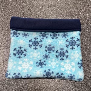 May include: A blue and white fleece pet bed with a snowflake pattern. The bed has a navy blue fleece trim around the top edge.