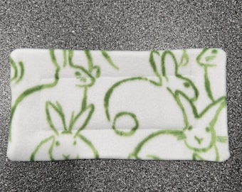 May include: White fleece fabric with a green outline of multiple rabbits. The rabbits are in various poses and sizes.