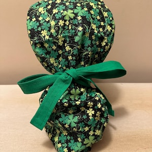 May include: A green and black scrub hat with a shamrock pattern. The hat has a green tie that is tied in a bow.