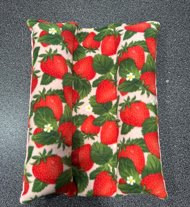 May include: A pink and white fabric pillow with a strawberry print. The pillow is divided into three sections and is filled with a soft material.