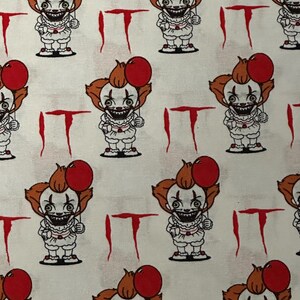K&ouml;nnte beinhalten: Wei&szlig;er Stoff mit einem sich wiederholenden Muster eines Pennywise-Cartoons aus dem Film ES. Pennywise h&auml;lt einen roten Ballon und hat ein bedrohliches L&auml;cheln. Die Worte "ES" sind in Rot auf den Stoff gedruckt.