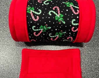 Könnte beinhalten: Ein rotes und schwarzes zylindrisches Haustierbett mit einem Zuckerstangenmuster. Das Bett hat ein rotes Fleecefutter und wird mit einem separaten roten Fleecekissen geliefert.