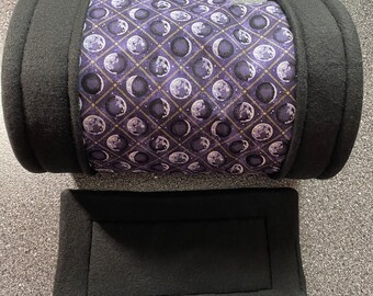 May include: A black fleece-lined cylindrical pet bed with a purple and gold moon phase print. The bed is accompanied by a matching black fleece-lined rectangular cushion.