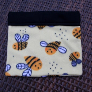 May include: A yellow fleece fabric pouch with a black fabric top. The pouch is decorated with a repeating pattern of cartoon bees.