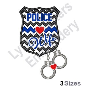 Könnte beinhalten: Schwarz-weißes Chevron-Polizeibadge mit einem blauen Streifen und einem roten Herzen. Das Abzeichen lautet "Police Wife" und ist an ein Paar silberne Handschellen mit einem roten Herz-Anhänger befestigt.