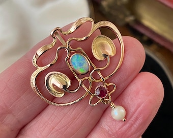 May include: A gold pendant with an opal, ruby, and pearl. The pendant is in an intricate design with a floral motif.