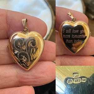 May include: A gold heart-shaped locket featuring an engraved floral pattern on the front and the inscription I will love you more tomorrow than today on the back. The piece includes a small metal bail and visible hallmarks stamped on the surface.