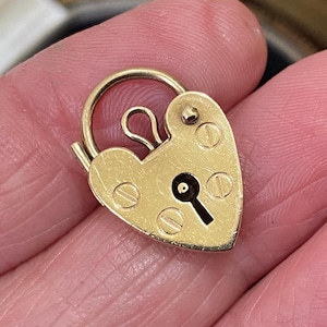 Puede incluir: Un candado dorado en forma de corazón con un ojo de cerradura y un asa curva. El candado tiene un ojo de cerradura y está asegurado con tornillos pequeños. El candado es una pieza vintage.