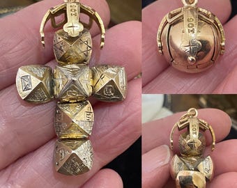 May include: A gold pendant in the form of a cross, featuring detailed geometric patterns and a hinged design. The pendant includes a loop for a chain. The cross is constructed from multiple cube-shaped components.