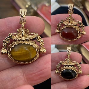 Puede incluir: Tres colgantes dorados con diseños ornamentados y piedras preciosas ovaladas. Un colgante presenta una piedra ojo de tigre, otro una piedra marrón rojiza y el tercero una piedra negra. Los colgantes tienen una argolla decorativa en la parte superior.