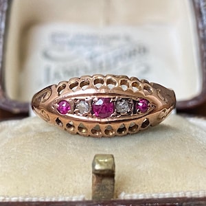 May include: A rose gold ring featuring an elongated, openwork gallery design. The center of the band is set with a row of five alternating stones, including three round, vibrant pink rubies and two clear, sparkling white diamonds.
