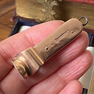 May include: A gold-toned metal charm with a loop at the top. The charm is shaped like a small, elongated rectangle with rounded edges. The charm has a small, round dot on one side and the inscription "925" on the other side.
