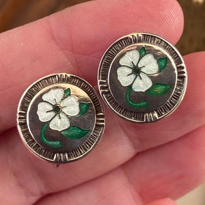 May include: A pair of silver tone clip-on earrings with white enamel flowers and green enamel leaves.