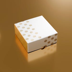 May include: A white gift box with gold floral pattern on the sides and top. The box is closed and sits on a gold surface. The box has a small circular opening on the side.