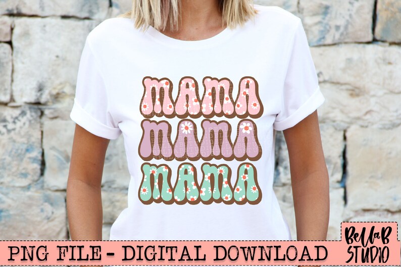 May include: White t-shirt with the word "MAMA" in three rows, each in a different color and design. The top row is pink with white flowers, the middle row is purple with white flowers, and the bottom row is teal with white flowers.