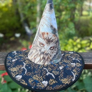 May include: A conical hat featuring a detailed owl face print on the crown and a quilted dark blue brim decorated with a repeating pattern of small white owls and golden foliage, finished with a solid black fabric trim along the outer edge.