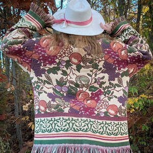 May include: A tapestry jacket with a floral pattern in shades of burgundy, green, and peach. The jacket has a fringed hem and sleeves. A white hat with a pink ribbon is also visible.