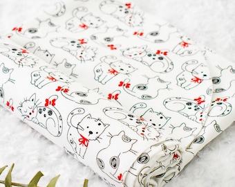 May include: White fabric with a repeating pattern of black and white cats with red bows. The fabric is rolled up and the edges are visible.
