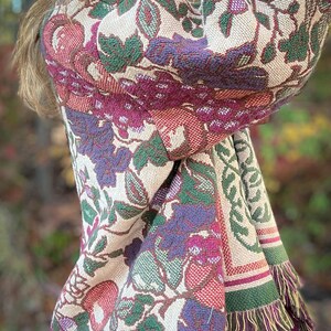 May include: A woven tapestry shawl with a floral pattern in shades of cream, green, purple, and red. The shawl features a fringed edge and a repeating botanical design. The fabric appears to be thick and textured, suitable for cooler weather.