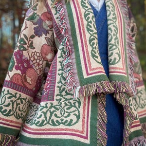 May include: A tapestry jacket with a floral and geometric pattern in shades of beige, green, burgundy, and purple. The jacket has a fringed hem and edges. The design includes botanical and ornamental elements.