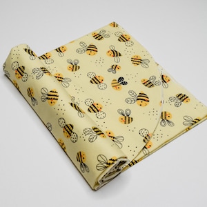 May include: A yellow fabric with a repeating pattern of black and yellow bees. The fabric is rolled up and the pattern is visible on both sides of the roll.