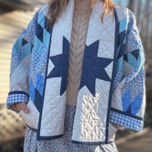May include: A white quilted jacket with a blue and white patchwork design. The jacket has a large navy blue star on the front and a gingham pattern on the cuffs.