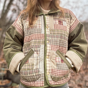 May include: A quilted jacket with a patchwork design. The jacket features a mix of plaid and solid fabric patches in shades of red, green, and cream. The sleeves are a solid olive green corduroy, and the jacket has two front pockets and a button closure.
