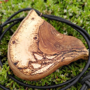 May include: A wooden pendant with a unique, natural wood grain pattern. The pendant is attached to a black leather cord.