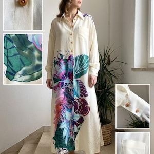 Può includere: Un abito camicia a maniche lunghe color crema con chiusura a bottoni, taschino sul petto e una stampa botanica nei toni del verde, viola e blu. L'immagine mostra dettagli dei bottoni marroni e dei polsini delle maniche dell'indumento.