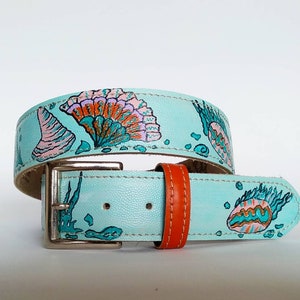 Könnte beinhalten: Ein hellblauer Ledergürtel mit handgemaltem Design von Muscheln in Rosa-, Orange- und Grüntönen. Der Gürtel hat eine silberne Schnalle und ein orangefarbenes Lederfutter.