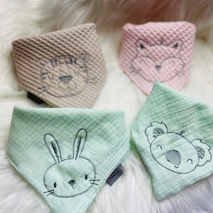 Könnte beinhalten: Vier Baby-Lätzchen mit verschiedenen Tiermotiven. Die Lätzchen sind aus weichem, strukturiertem Stoff und in den Farben Rosa, Beige und Grün gehalten. Die Tiere sind ein Tiger, eine Katze, ein Koala und ein Kaninchen.