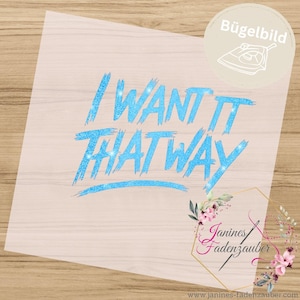 Könnte beinhalten: Ein hellblaues Glitzer-Bügelbild mit dem Text I WANT IT THAT WAY in Pinselstrich-Schriftart. Das Design enthält ein kreisförmiges Symbol mit einer Bügeleisen-Grafik und dem Wort Bügelbild sowie ein florales Logo von Janines Fadenzauber.