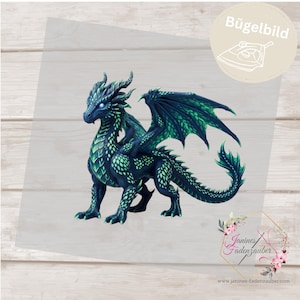 Könnte beinhalten: Ein Bügelbild mit einem detaillierten Drachen mit dunkelblauen und leuchtend grünen Schuppen, strahlend weißen Augen und großen Flügeln. Das Design enthält den Text Bügelbild, ein Bügeleisensymbol sowie das Logo von Janines Fadenzauber.