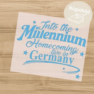 Op de afbeelding: Een lichtblauwe opstrijkbare transfer met de tekst "Into the Millennium Homecoming live in Germany" in een gestileerd lettertype, versierd met kleine sterretjes en een gebogen onderstreping op een transparant vel.