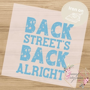 Könnte beinhalten: Ein hellblaues Bügelbild mit dem abgenutzten Text BACK STREET'S BACK ALRIGHT. Das Design enthält ein kreisförmiges Abzeichen oben rechts mit dem Text Iron on und einem Bügeleisensymbol sowie eine florale Grafik in der unteren rechten Ecke.