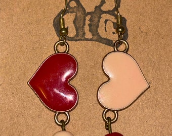 May include: A pair of dangle earrings with heart-shaped charms. One charm is red and the other is pink. Each charm has a small bead dangling from it. The red bead is attached to the pink heart and the white bead is attached to the red heart.
