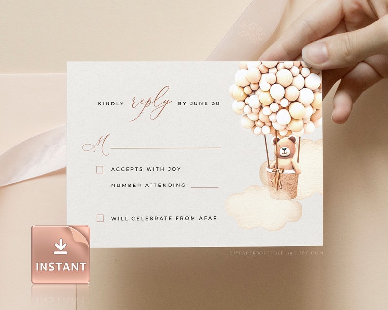 May include: A white RSVP card with a brown teddy bear in a hot air balloon made of beige and white balloons. The card has a gold line and the text "KINDLY reply BY JUNE 30". There are two checkboxes with the text "ACCEPTS WITH JOY" and "WILL CELEBRATE FROM AFAR".