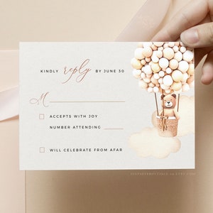 May include: A white RSVP card with a brown teddy bear in a hot air balloon made of beige and white balloons. The card has the text "KINDLY reply BY JUNE 30" and two checkboxes: "ACCEPTS WITH JOY" and "WILL CELEBRATE FROM AFAR".