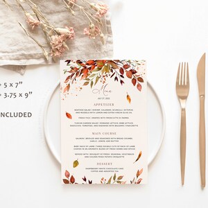 May include: A fall-themed wedding menu card with watercolor leaves in shades of orange, red, and yellow. The menu includes appetizer, main course, and dessert options. The text on the card reads "Menu" and "July 27, 2022".