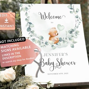 May include: Welcome to Jennifer's Baby Shower sign with a watercolor background featuring a cute teddy bear holding a heart-shaped balloon. The sign is decorated with eucalyptus leaves and has the date September 14th, 2022.