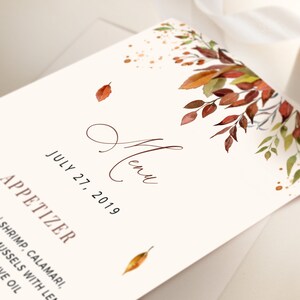 May include: A wedding menu card with a watercolor illustration of fall leaves in shades of red, orange, and yellow. The text on the card reads "Menu" and "July 27, 2019".