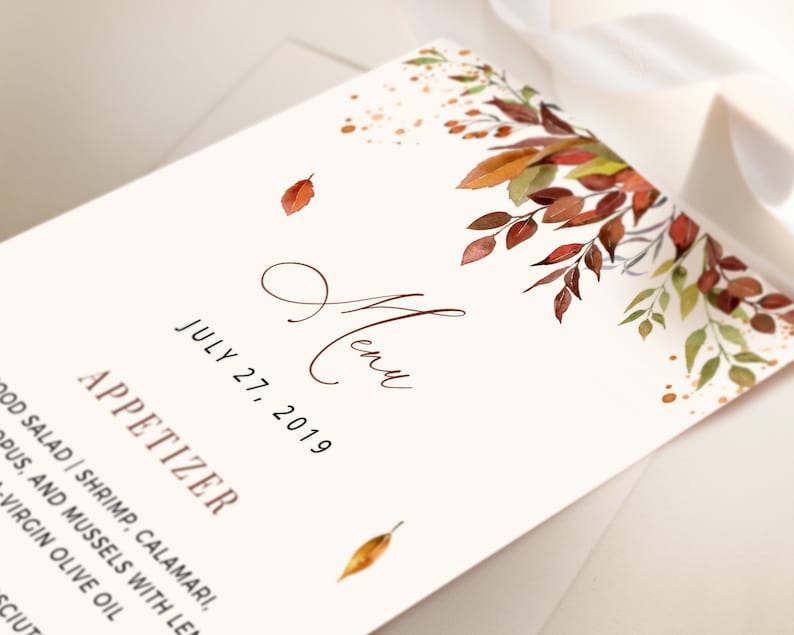 May include: A wedding menu card with a watercolor illustration of fall leaves in shades of red, orange, and yellow. The text on the card reads "Menu" and "July 27, 2019".