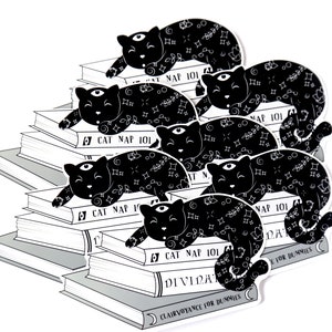 Puede incluir: Una pila de libros con ilustraciones en blanco y negro de gatos durmiendo encima. Los libros tienen t&iacute;tulos como "Cat Nap 101" y "Clarividencia para Dummies".
