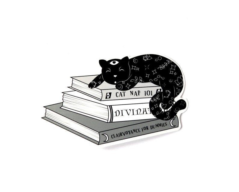 Puede incluir: Un gato negro con un tercer ojo y un patr&oacute;n de estrellas duerme encima de una pila de tres libros. Los libros se titulan "Cat Nap 101", "Divinaci&oacute;n" y "Clarividencia para Dummies".