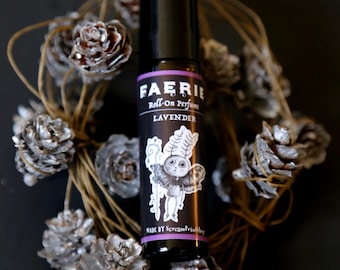 May include: A black roll-on perfume bottle with a white label that says "FAERIE Roll-On Perfume LAVENDER" and a cartoon illustration of a fairy. The bottle is surrounded by a wreath of pine cones.