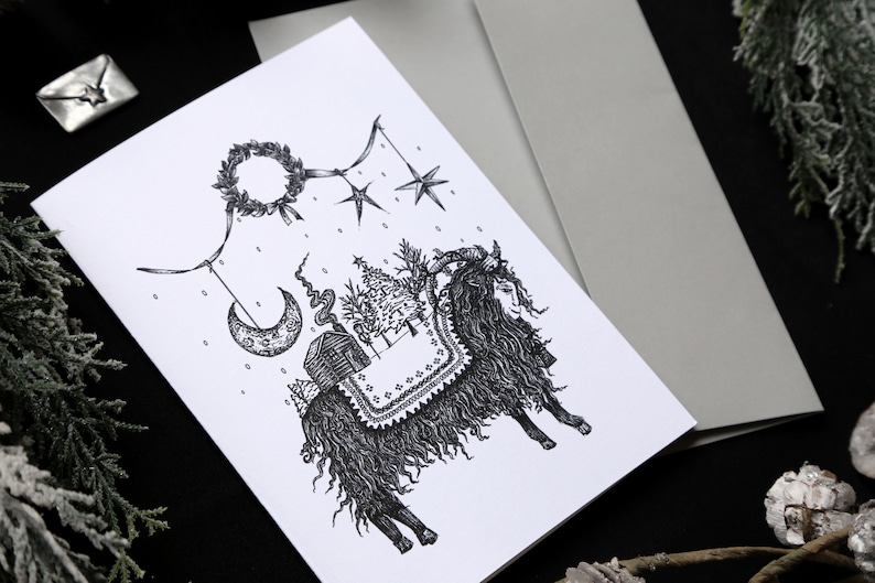 May include: A black and white illustration of a goat with a wreath, stars, a crescent moon, and a small house hanging from a string. The goat is standing on a snowy ground with a pine tree in the background.