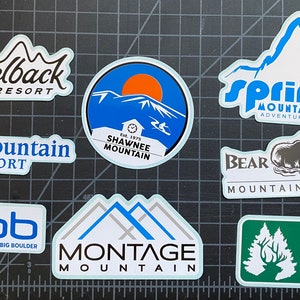 May include: A collection of nine colorful ski resort stickers featuring mountain scenes, logos, and names. The stickers include Camelback Resort, BlueMountain Resort, Shawnee Mountain, Spring Mountain Adventures, Bear Creek Mountain Resort, JFbb Jack Frost Big Boulder, Montage Mountain, and Elk Mountain.