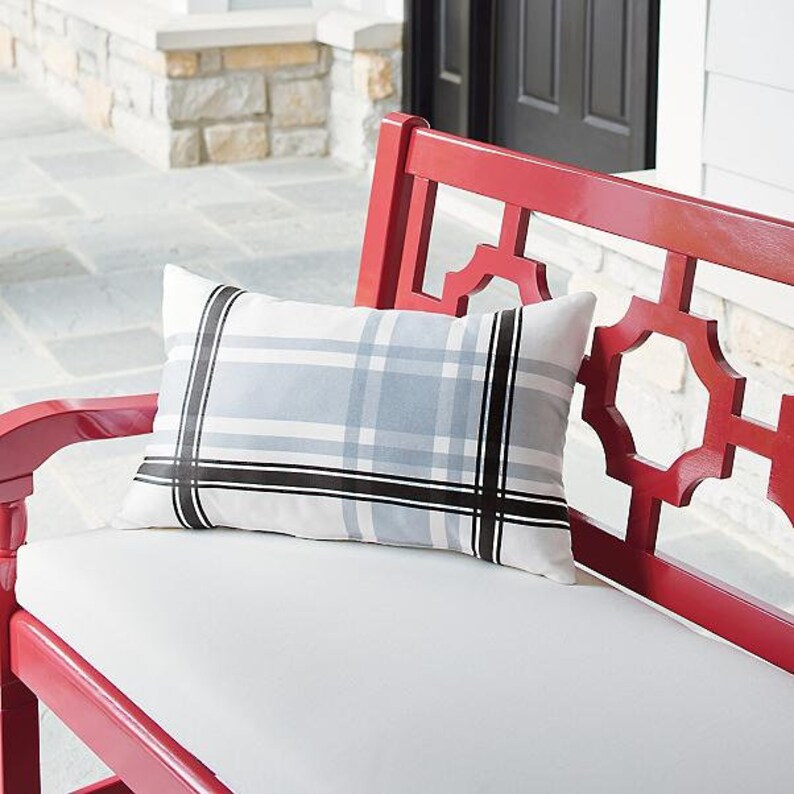 May include: A rectangular outdoor pillow with a plaid pattern in white, light blue, and black. The pillow is placed on a white cushion of a red bench. The bench has a decorative back.