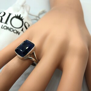 May include: A silver ring with a large, dark blue gemstone. The ring is set with a rectangular stone and has a simple, elegant design.