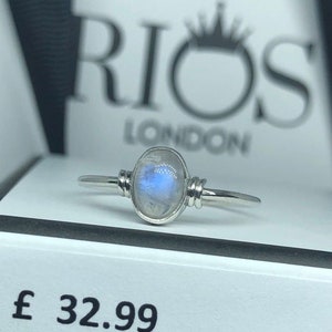 May include: A silver ring with a round, iridescent moonstone. The ring is set on a white box with the text "RIOS LONDON" and the price "£ 32.99".